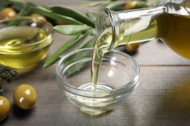 Kâseye zeytinyağı dökerek ve zeytinleri ahşap masaya dökerek, yakından. Sağlıklı yemek.