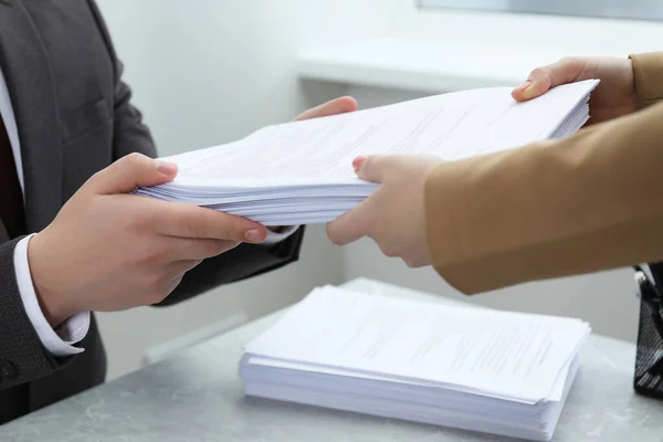 Woman giving many documents to man at table in office, closeup