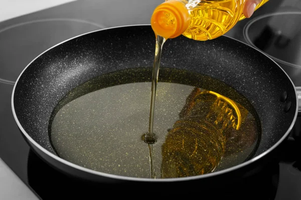 Woman pouring cooking oil into frying pan on stove, closeup