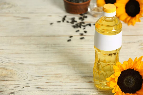 Sunflower cooking oil and yellow flowers on white wooden table, space for text