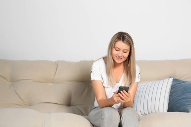 Evdeki koltukta akıllı telefon kullanan bir kadın. Metin için boşluk