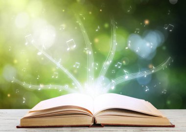 Kitaptan müzik akıyor. Beyaz ahşap masada bulanık arka planda müzik sembolleri uçuşuyor.