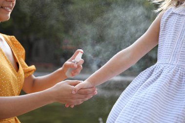 Anne, dışarıdaki kızın eline böcek kovucu sürüyor, yakın plan.