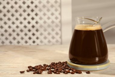 Sıcak içecek ve ahşap masada fasulye bulunan cam Türk kahve demliği, mesaj için yer.