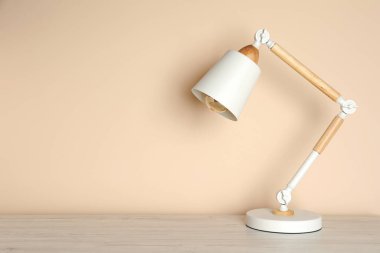 Modern masa lambası bej duvarın yanındaki beyaz ahşap masa üzerinde, metin için yer var.
