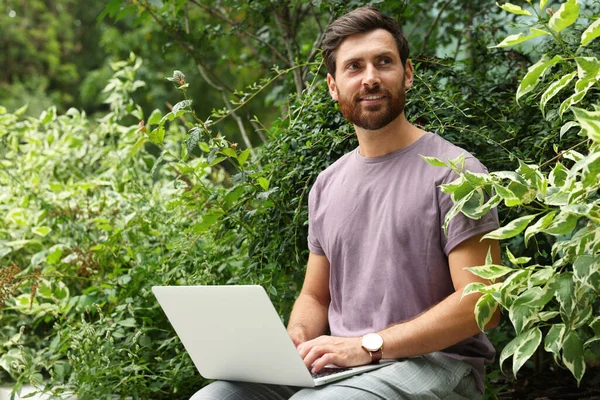 Handsome man with laptop in green garden