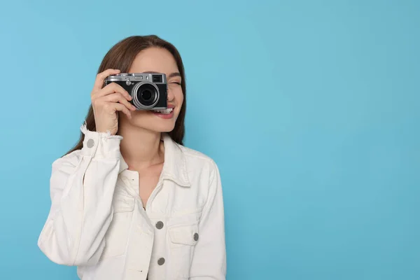 Young woman with camera taking photo on light blue background, space for text. Interesting hobby