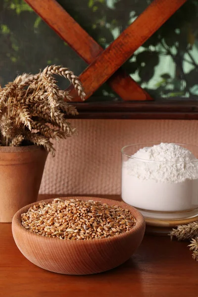 Wheat grains in bowl, spikes and flour on wooden table