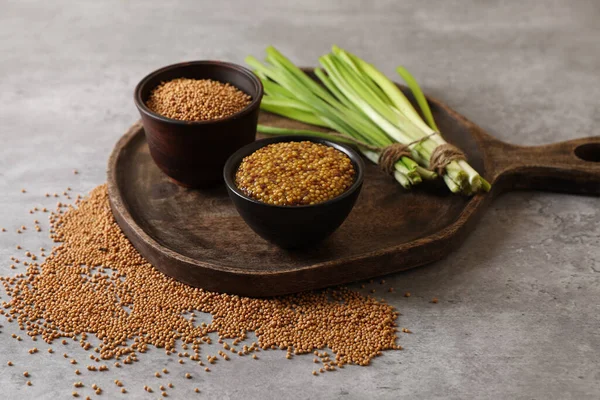 Serving board with delicious whole grain mustard, seeds and fresh green onion on grey table