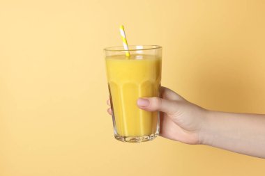 Sarı arka planda bir bardak lezzetli smoothie tutan kadın, yakın plan.