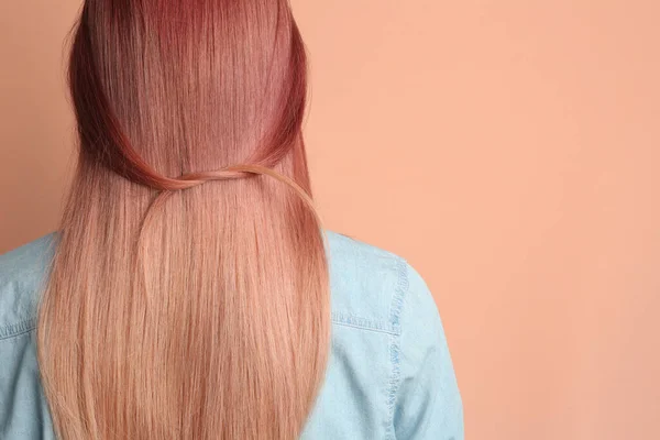 Woman with bright dyed hair on pale pink background, back view. Space for text