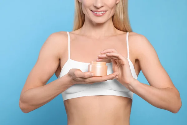 Woman with jar of body cream on light blue background, closeup