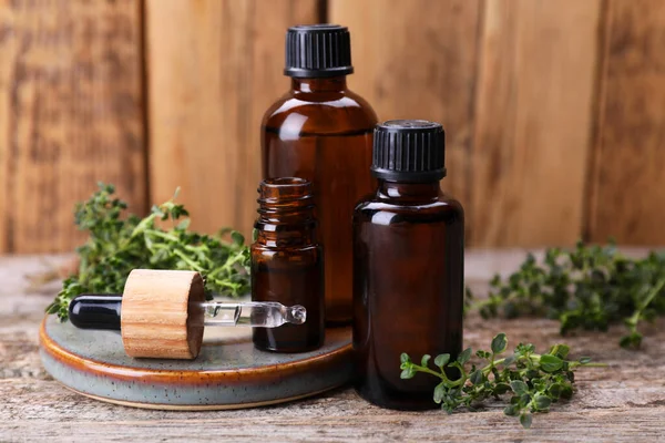 Bottles of thyme essential oil and fresh plant on wooden table