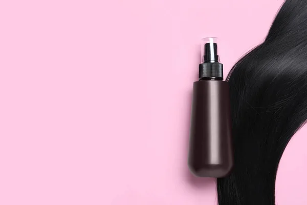 Spray bottle with thermal protection and lock of black hair on pink background, flat lay. Space for text