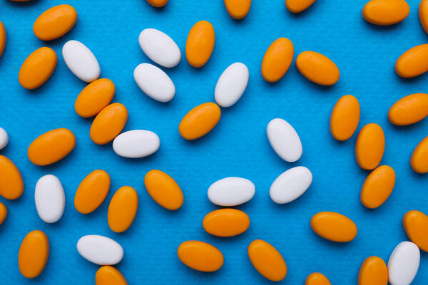 Many bright dragee candies on blue background, flat lay