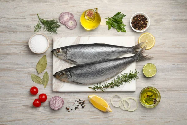 Delicious salted herrings and different ingredients on light wooden table, flat lay