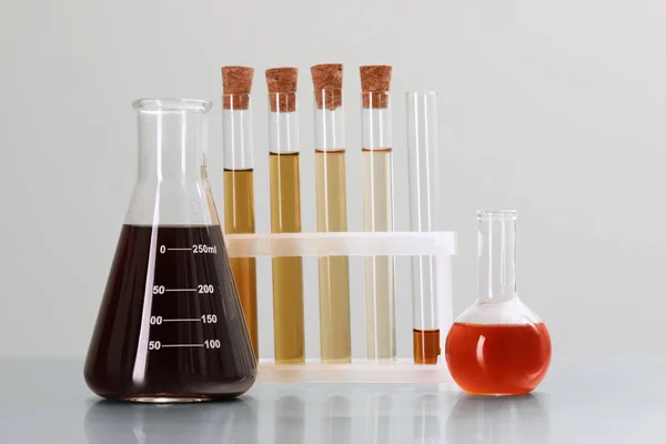 Different laboratory glassware with brown liquids on table against light background