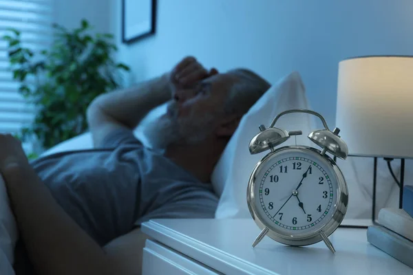 Sleepy man in bed at home, focus on alarm clock. Space for text