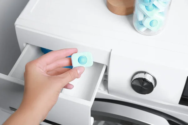 Woman putting water softener tablet into washing machine, closeup