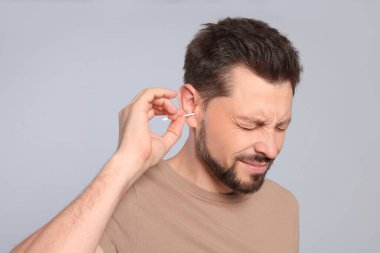 Man cleaning ears and suffering from pain on grey background clipart