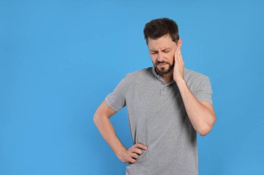 Açık mavi arka planda kulak ağrısı çeken bir adam.