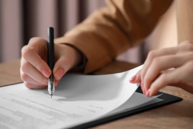 Ofisteki ahşap masada belgeleri imzalayan kadın, yakın plan.