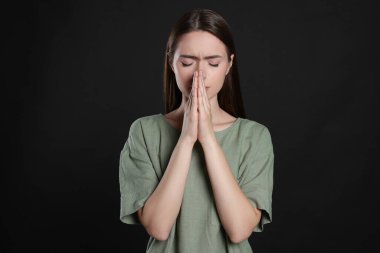 Elleri sımsıkı bağlı bir kadın siyah arka planda dua ediyor.