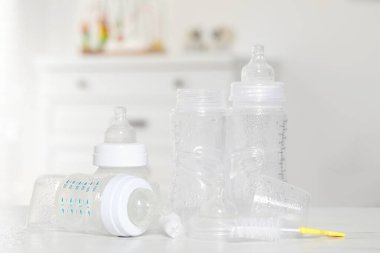 Sterilizasyondan sonra meme uçları olan temiz bebek şişeleri ve beyaz masadaki temizlik fırçası.