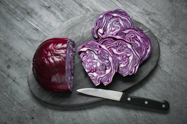 Taze olgun kırmızı lahana dilimleri ve bıçak gri masada, düz yatıyordu.