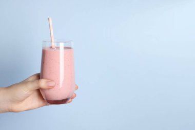 Açık mavi arka planda bir bardak lezzetli smoothie tutan kadın, yakın plan. Metin için boşluk