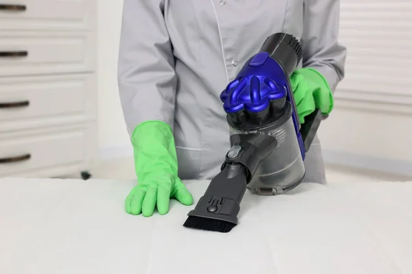 Woman in gloves disinfecting mattress with vacuum cleaner indoors, closeup
