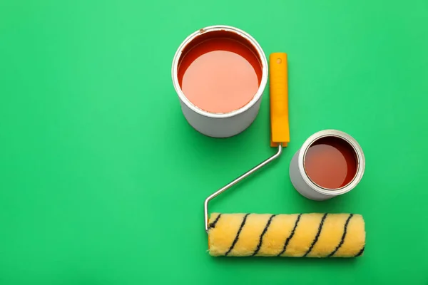 Cans of orange paint and roller brush on green background, flat lay. Space for text