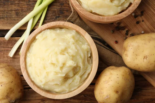 Bowls of tasty mashed potato, pepper and leeks on wooden table, flat lay