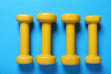 Açık mavi arka planda sarı dambıllar, düz. Sabah egzersizi