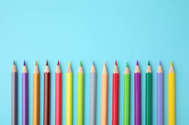 Açık mavi arka planda renkli ahşap kalemler, düz bir zemin. Metin için boşluk