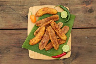 Lezzetli kızarmış muzlar, farklı biberler ve ahşap masa üzerinde limon dilimleri.