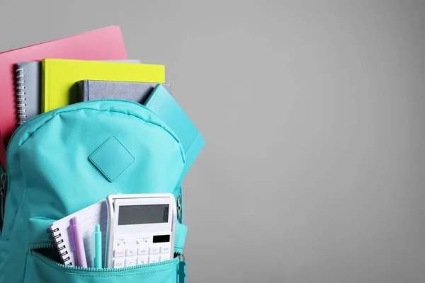 Turquoise backpack and different school stationery on grey background, space for text