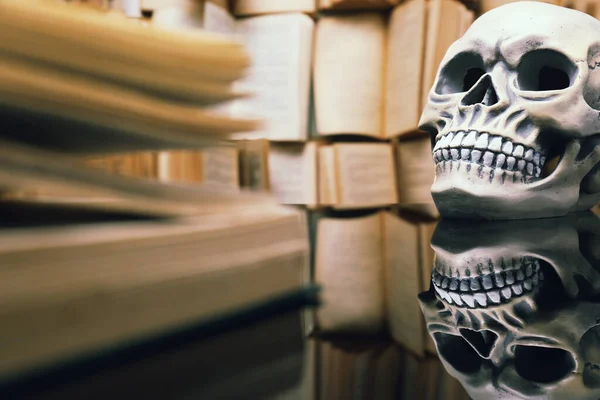 Human skull and old book on mirror table