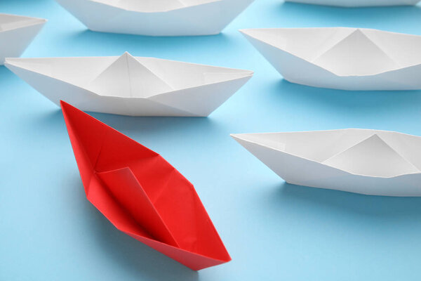 Red paper boat among others on light blue background, closeup. Uniqueness concept