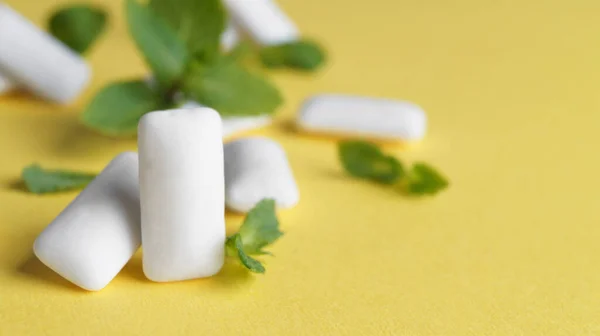 Tasty chewing gums and mint leaves on yellow background, closeup. Space for text