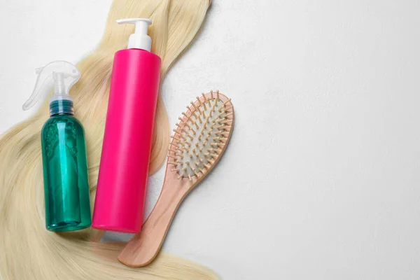 Spray bottles with thermal protection, lock of blonde hair and hairbrush on white background, flat lay. Space for text