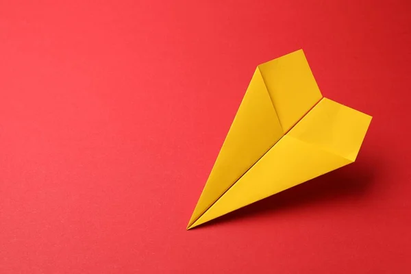 Handmade yellow paper plane on red background, space for text