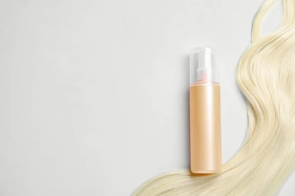 Spray bottle with thermal protection and lock of blonde hair on light background, flat lay. Space for text