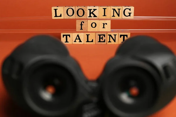Staff recruitment concept. Phrase Looking For Talent made of wooden cubes and binoculars on orange background, selective focus
