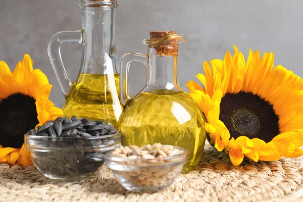 Sunflower cooking oil, seeds and yellow flowers on wicker mat, closeup