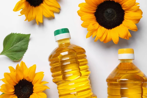 Bottles of cooking oil and sunflowers on white table, flat lay