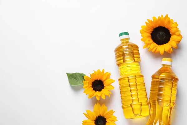 Bottles of cooking oil and sunflowers on white table, flat lay. Space for text