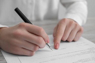 Ofisteki ahşap masada belgeleri imzalayan kadın, yakın plan.