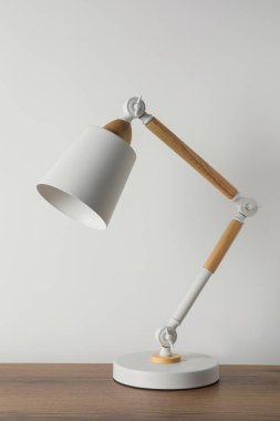 Beyaz duvarın yanındaki ahşap masada modern masa lambası.