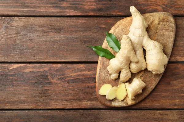 Cut and whole fresh ginger with leaves on wooden table, top view. Space for text